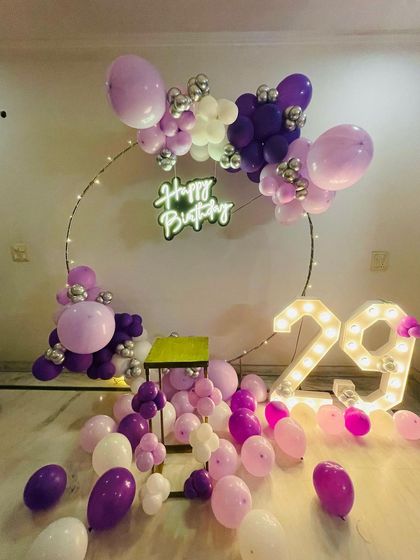 A purple and pink themed 29th birthday. This setup features a circular balloon frame, scattered balloons on the floor, and large light-up numbers.