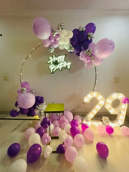A purple and pink themed 29th birthday. This setup features a circular balloon frame, scattered balloons on the floor, and large light-up numbers.