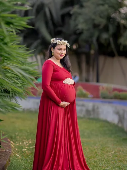 A classic solo maternity pose, with the mom-to-be looking radiant in her red gown and floral crown.