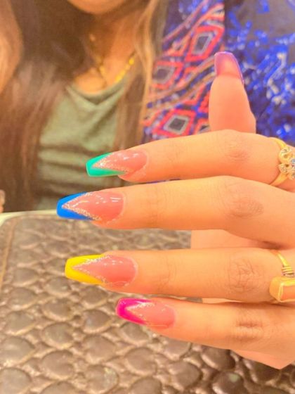 A close-up of a colorful and modern French manicure. The V-shaped tips are painted in different neon colors, with a line of silver glitter for extra definition.