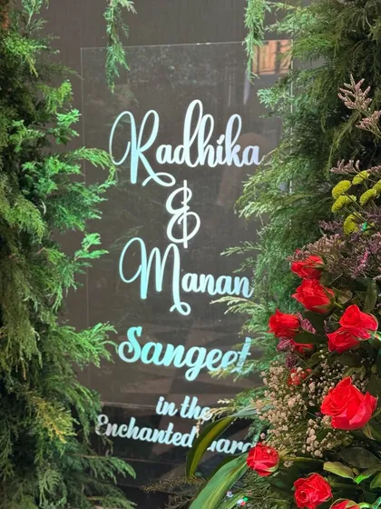 Customised entrances with calligraphy fonts and a touch of LED light to mark the perfect welcome. This sign for the "Enchanted Garden" sangeet is nestled in a bed of greenery. 💡