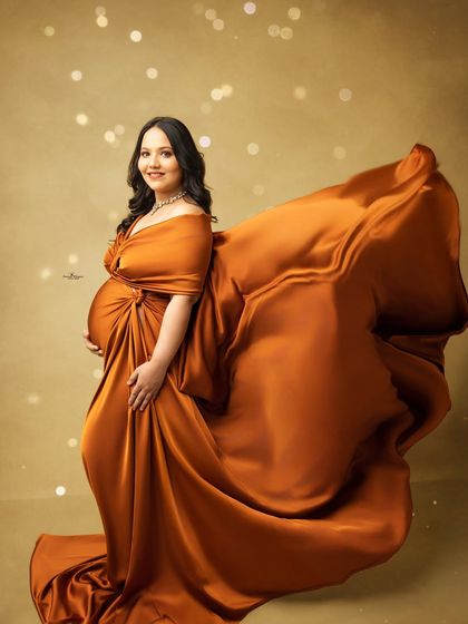 A stunning solo portrait featuring a dramatic flying fabric effect. The mother-to-be looks powerful and radiant as the rust-colored gown flows behind her.