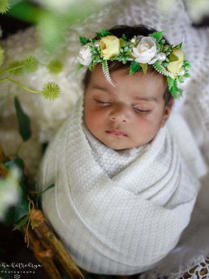 A touch of nature with this beautiful floral crown. The baby is wrapped in a simple white cloth, letting the delicate headgear and greenery shine.
