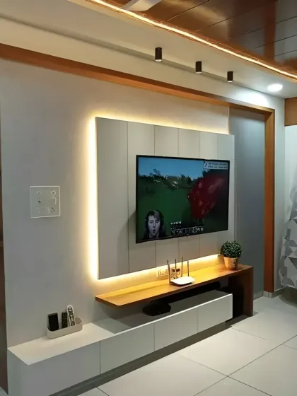 A simple yet effective TV wall design with a floating console and a backlit panel. The wood-paneled ceiling with track lighting adds warmth and directs attention to the entertainment zone.