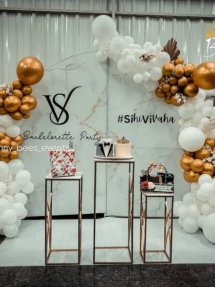 We design stylish bachelorette parties that are perfect for the gram. This setup features a trendy marble-print backdrop, a custom balloon arrangement in gold and white, and personalized signage with the couple's hashtag.