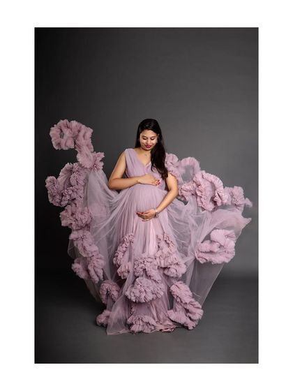 A breathtaking shot of a mother-to-be in a dramatic lavender ruffled gown. The fabric appears to float around her, creating an ethereal and angelic portrait that looks like a work of art.