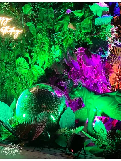 Details make the theme. For a "Neon Jungle" party, I combined a massive disco ball with a custom neon 'Happy Birthday' sign and animal props, all bathed in dramatic green and purple light to create a wild, glamorous photo corner.