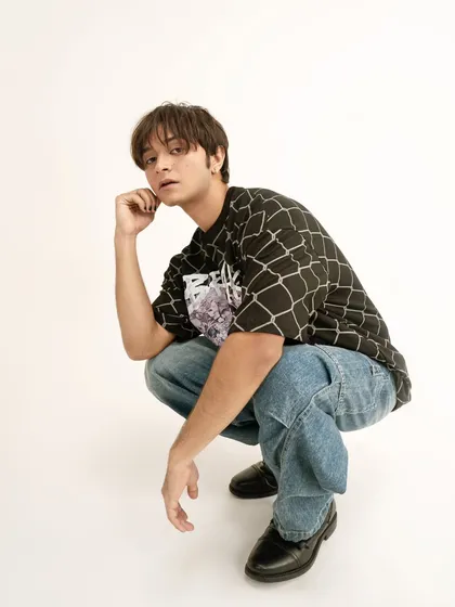 A casual, full-body shot for a streetwear brand. The crouching pose and direct gaze feel authentic and cool, perfectly capturing the vibe of oversized, graphic tees.