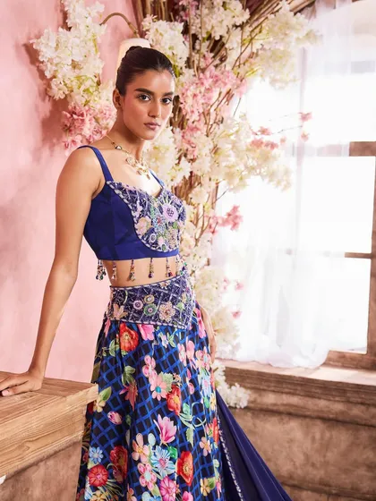 A standing portrait showcasing a floral embroidered bustier and lehenga. The makeup features a defined eye and a soft pink lip, adding a touch of glamour to the festive look.