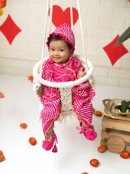 A sweet seven-month-old celebrating Raja Parba in a traditional pink outfit on a decorated swing.