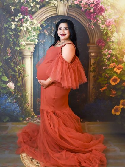 A smiling portrait of a mom-to-be in a rust-colored gown against our floral arch backdrop.