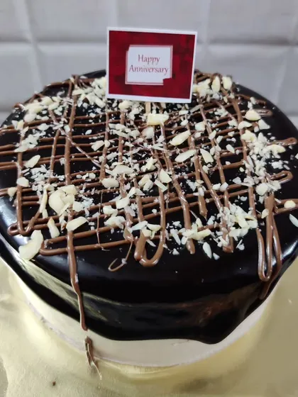 A delicious chocolate anniversary cake topped with a rich ganache drip, chocolate drizzle, and chopped nuts.