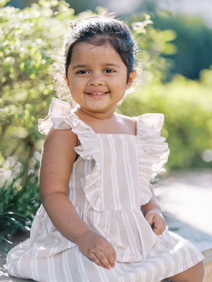 A beautiful portrait of a little girl in a striped dress, smiling in the sunshine. The natural light is perfect for capturing her happy expression.