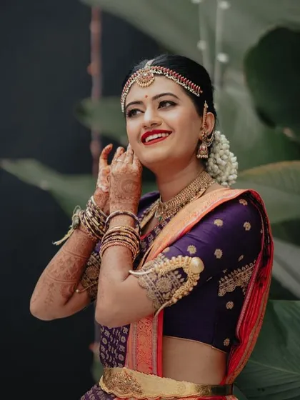 A bride in a purple and orange Kanchipuram saree. Her custom purple blouse features unique armlet-style embroidery on the sleeves.