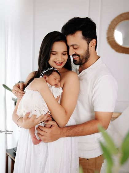 A lovely family photo from a newborn session. The parents are all smiles as they cradle their sleeping baby, dressed in coordinated white outfits for a clean and timeless look.