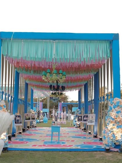 A grand entrance tunnel for an outdoor carnival party. The walkway is decorated with colorful ceiling drapes, chandeliers, and a custom printed floor.