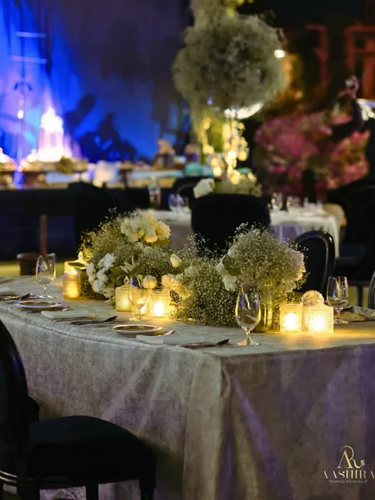 A beautiful dining table setup with a runner of baby's breath and white roses, illuminated by the warm, soft glow of numerous candles.