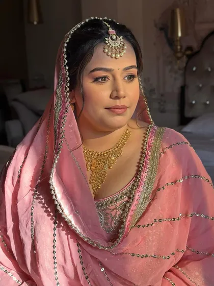 The golden hour light hitting her face perfectly. Her makeup is soft and glowing, with peachy tones that complement her pink pastel outfit.