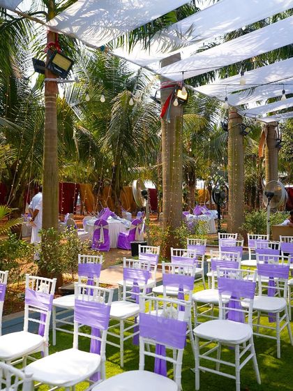 An outdoor ceremony setup with a lovely lavender color scheme. The white chairs with lavender sashes and the lush green lawn create a fresh and elegant look for a daytime wedding.