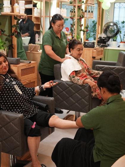 A candid moment of clients enjoying a group pampering session. While one receives a foot massage, another gets a relaxing shoulder rub, all within our open and social salon environment.