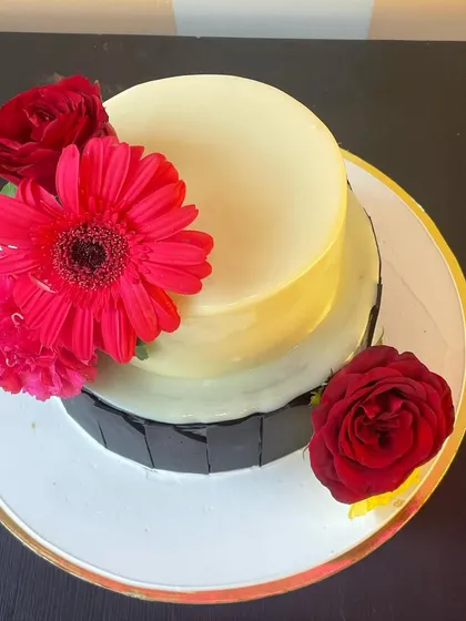 An overhead view of the two-tier cake, showing the artistic arrangement of the bright gerbera daisy and roses against the smooth white and dark chocolate surfaces.