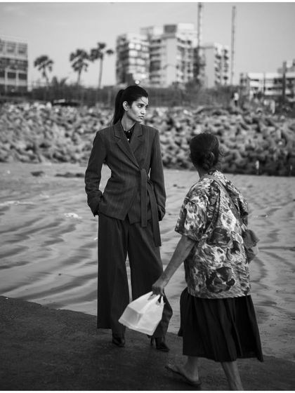 A candid, documentary-style black and white shot that places high fashion in an everyday context. This image tells a story of two worlds meeting on the beach.