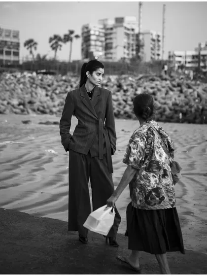 A candid, documentary-style black and white shot that places high fashion in an everyday context. This image tells a story of two worlds meeting on the beach.
