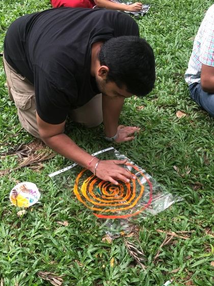 A participant creating a spiral art piece on the grass. Our activities encourage connecting with the earth as we create.
