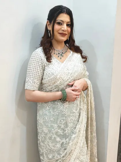 A beautiful wedding guest look in a classic white saree. The hair is styled in a half-updo with soft curls, a timeless choice that complements her diamond and emerald jewelry.