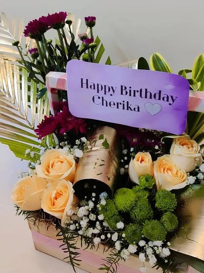 A detailed shot of the birthday basket, focusing on the textures of the different flowers and the elegant way the champagne bottle is integrated into the design.