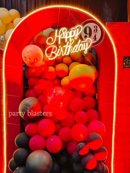 A glowing archway with a "Happy Birthday" neon sign and the Platform 9 3/4 logo. The cascading red, yellow, and black balloons perfectly match the Gryffindor house colors.