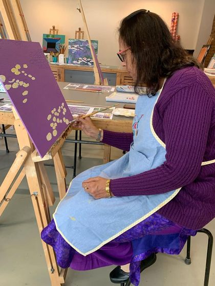 An artist begins her Monet painting, carefully placing the first water lilies on a rich purple background.