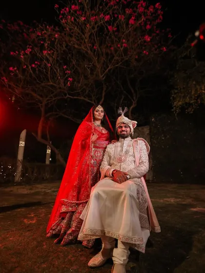 A majestic portrait of the bride and groom on their wedding night. The groom is seated while the bride stands beside him, creating a classic, royal pose.