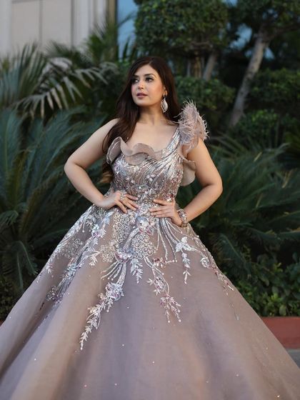 A client posing in the rose-gold organza gown against a backdrop of lush greenery. The natural setting highlights the dress's delicate colors and details.