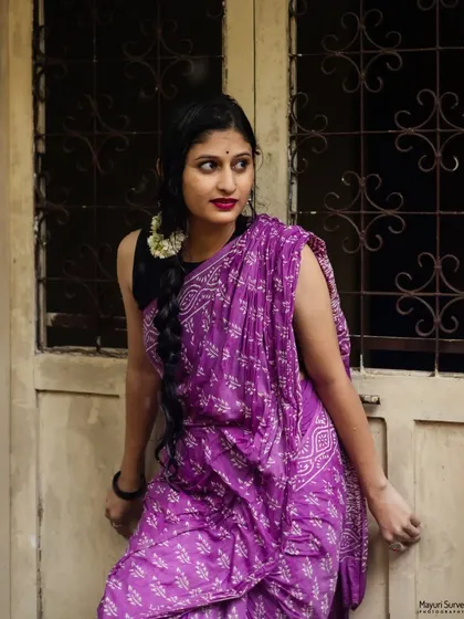 A classic pose against an old-world door with intricate grilles. The model's expression is poised and direct, and the setting adds a vintage charm to this ethnic portrait in a purple saree.
