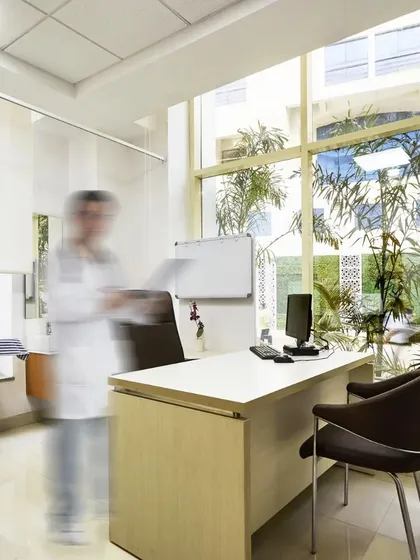 This consultation room at Ramkrishna Care Hospital is bright and modern, with a large window providing natural light and a view of the campus greenery. The design creates an understated and professional environment.