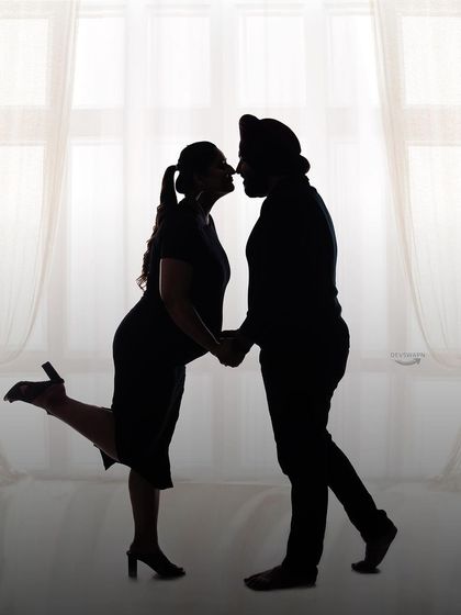 A romantic silhouette of a couple against a bright window. The playful leg kick adds a touch of fun and personality to this classic and intimate pose.