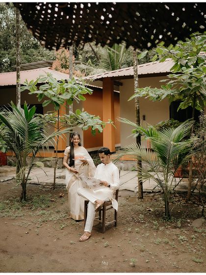 A classic portrait in a traditional courtyard. He sits reading the paper while she stands by his side, a timeless depiction of companionship and quiet love.