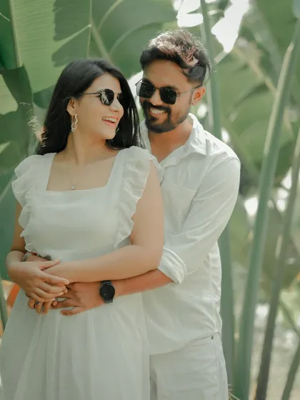 A fun and carefree moment captured against a backdrop of lush tropical leaves. The couple, dressed in matching white, shares a laugh, showcasing the relaxed and joyful side of their relationship.