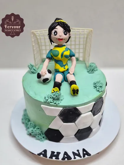 A football theme cake celebrating a female player. This cake features a hand-crafted fondant figure of a girl in her football jersey, sitting on a field with a soccer ball.