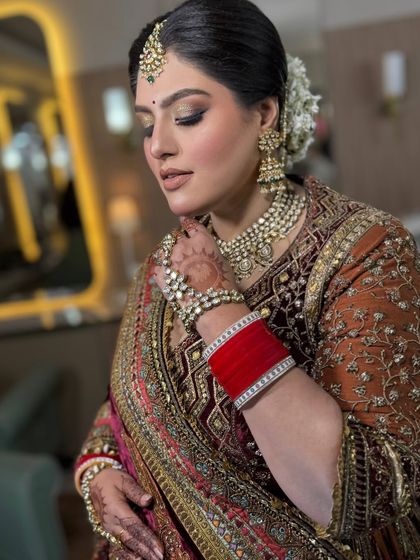 This bride looks absolutely regal in her velvet lehenga. The makeup is soft and glowing, with a classic white floral bun adding a touch of freshness to the overall look.