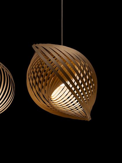 A close-up of the Adilo pendant, its swirling form creating a captivating sense of movement. The light from within highlights the natural grain of the Finnish birch.