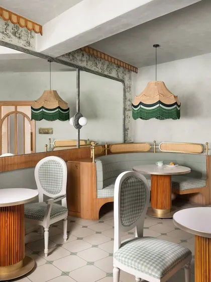 An overview of the custom-designed seating area, with its curved gingham-upholstered booth, cane-back railing, and fluted-base tables. Every piece was crafted to tell a cohesive story.