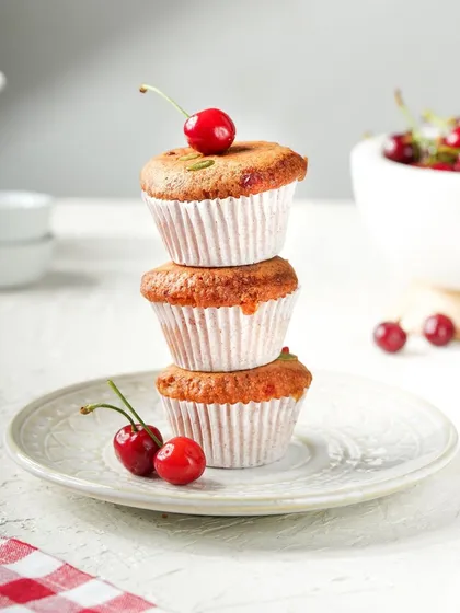 A playful stack of three cherry-topped muffins. The bright, clean background and simple styling make this a classic and appealing shot for any bakery.