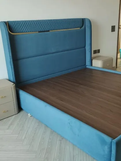 A luxurious bed upholstered in a vibrant blue velvet, featuring a headboard with quilted detailing and gold trim. This piece is designed to make a bold statement, combining rich color with sophisticated accents.