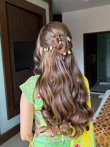 A back view of the intricate Haldi hairstyle, with a woven bun and colorful floral accessories scattered throughout the waves.