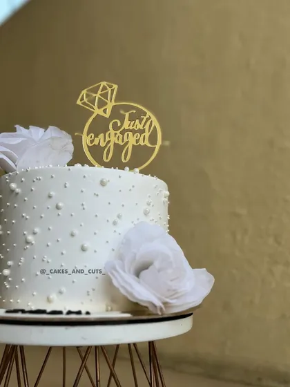 A close-up of our pearl-dotted engagement cake with white flowers and a "Just Engaged" topper. The details create a delicate and sophisticated look.