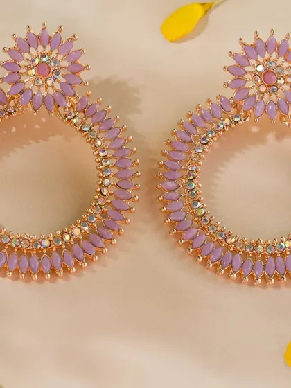 A pair of large, lavender-colored statement earrings. The soft, silky background and scattered petals add a touch of elegance and femininity.