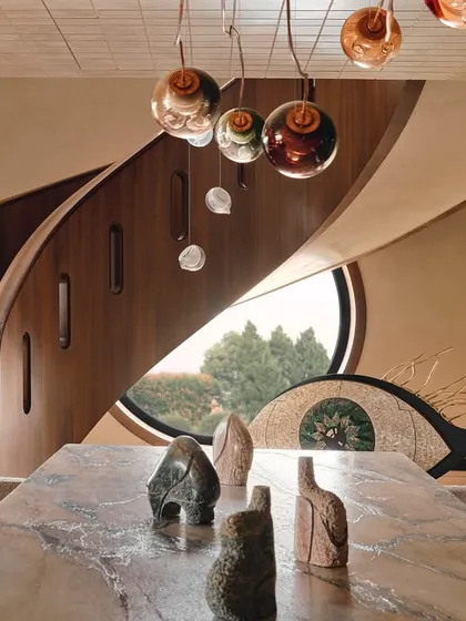 A view across the dramatic stone dining table towards the spiral staircase. This image captures the essence of the home: a blend of powerful natural materials, sculptural forms, and artistic lighting.
