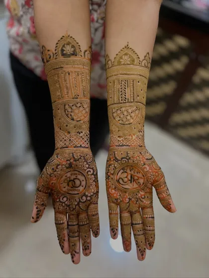 This engagement mehendi features the couple's initials and intertwined rings on the palms. The design continues up the arms with detailed bands and traditional Indian architectural motifs.